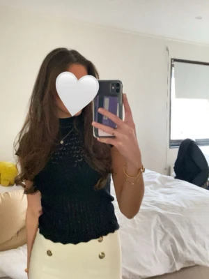 Svart stickad topp med spetsdetaljer från ZARA - Snygg svart stickad topp med korta ärmar och fina spetsdetaljer framtill. Toppen har en hög hals och är lätt genombruten vilket ger en trendig look. Perfekt att styla med både kjol och byxor för en chic outfit.