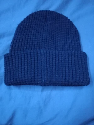 Svart ribbstickad mössa från K2 - Säljer en svart ribbstickad mössa från K2 med uppvikt kant och diskret logga på sidan. Mössan är gjord i ett tjockare, mjukt material som håller värmen bra. Perfekt för kalla dagar och enkel att matcha med olika stilar.