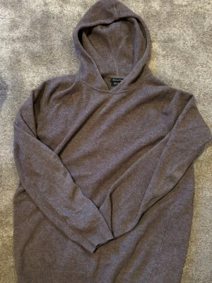 Brun hoodie i mjuk kashmir  - Säljer en stilren brun hoodie från Massimo dutti i mjuk kashmir. Hoodien har en klassisk huva, ribbade muddar vid ärmslut och nederkant samt en enkel, clean look utan tryck eller dragkedja. Perfekt för dig som gillar minimalistisk stil.