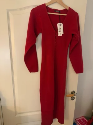 Röd stickad klänning med knappar - Snygg röd stickad kofta med dekorativa klädda knappar framtill och V-ringning. Mjuk och skön kvalitet, långärmad och i klassisk modell. Skulle komma till användning vid jul med blev inget av det men perfekt nu inför alla ❤️dag