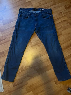 Mörkblå jeans från Replay - Snygga mörkblå jeans från Replay med klassisk femficksmodell och diskreta slitningar. Jeansen har slim ben och tydliga sömmar, samt Replay-logga på myntfickan. Perfekta för dig som gillar stilrena och tidlösa jeans. W34/L30