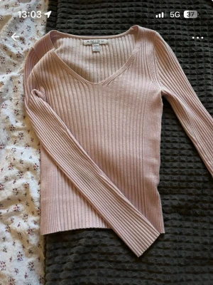 Två långärmade toppar i rosa och marinblå - Säljer två snygga långärmade toppar. Den ena är ljusrosa, ribbad och v-ringad från Ambition. Den andra är marinblå med spetsdetaljer vid v-ringningen. Perfekta att styla med jeans eller kjol för en trendig look.