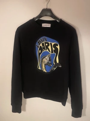 Svart sweatshirt Lanvin Paris - Cool svart sweatshirt från Lanvin med färgglatt tryck på bröstet där det står 'Lanvin Paris' och en grafisk häst. Tröjan har rund halsringning, långa ärmar och ribbade muddar. Perfekt för dig som gillar streetwear och vill sticka ut.