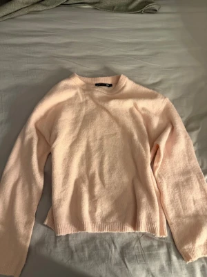 Ljusrosa stickad tröja från 157 - Mysig ljusrosa stickad tröja från 157 med rund halsringning och långa ärmar. Den är liten i storleken, den passar även mig som har S/M.  Tröjan har en enkel, rak passform och ribbade muddar vid ärmslut och nederkant. Perfekt för att hålla värmen under kyliga dagar.