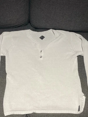 Stickad Tröja - Snygg vit stickad tröja från Blanc Du Nil med två knappar vid halsringningen och ribbade muddar. Tröjan har lång ärm och en klassisk, enkel design som passar till det mesta. Perfekt för dig som gillar stilrena plagg. Pris kan diskuteras, skriv om du har frågor.