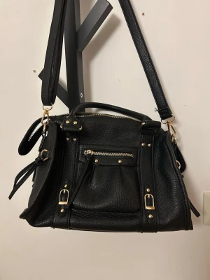 Svart handväska med gulddetaljer - Svart handväska med gulddetaljer. Väskan är ca 30x24. Använd 2-3 gånger.