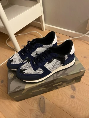 Valentino Rockrunners  - Snygga sneakers från Valentino i blått och vitt med svart detalj. Ovandelen är i mesh och mocka för en sportig look. Skorna har vita sulor och svarta skosnören. Perfekta för dig som vill ha en clean och modern stil. Nästan helt nya och alla tillbehöret medföljer!