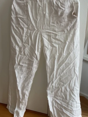 Vita linnebyxor med dragsko - Säljer ett par vita linnebyxor med avslappnad passform. Byxorna är tillverkade i ett lätt och luftigt linnetyg, perfekta för varma dagar. Klassisk rak modell utan synliga fickor framtill.