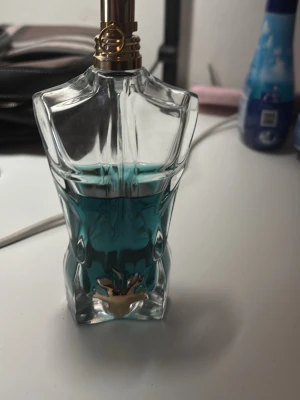 Jean Paul Gaultier Le Male parfym - Ikonisk parfymflaska formad som en manlig torso från Jean Paul Gaultier. Flaskan är genomskinlig med turkost blått innehåll och har detaljer i guld. Perfekt för dig som gillar unika och snygga parfymer att ha framme på hyllan.