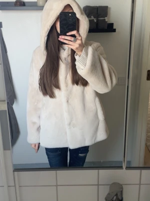Beige fluffig pälsjacka med luva - Säljer en supermjuk och fluffig beige pälsjacka med stor luva och knäppning framtill. Jackan har en avslappnad passform och två sidofickor. Knappen längst ner går ofta upp men inget som riktigt märks. Något märke från tidigare ägaren. 
