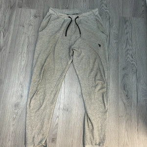 Grå mjukisbyxor från Polo - Säljer ett par grå mjukisbyxor med en Polo logga på sidan. Byxorna har en bekväm passform med snörning i midjan och sidofickor. Perfekta för en avslappnad stil.