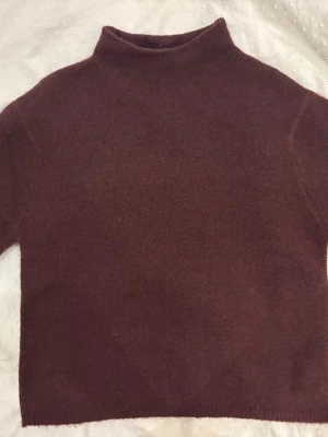 Brun stickad polotröja - Mysig vinröd stickad polotröja med rak passform och halvlånga ärmar. Tröjan har en hög krage och är tillverkad i ett mjukt, ull-liknande material. Perfekt för kyliga dagar och enkel att matcha med olika outfits. ALDRIG ANVÄND OCH I PERFEKT SKICK! 