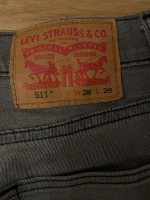 Grå Levi's 511 jeans W28 L29 - Säljer ett par grå Levi's 511 jeans med klassisk femficksdesign och smal passform. Jeansen har det ikoniska läderpatchen bak i midjan och är tillverkade i ett mjukt bomullsmaterial. Perfekta för en avslappnad och stilren look.