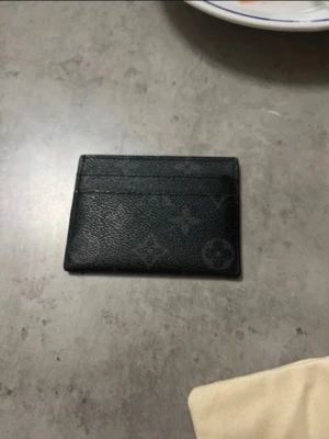 Svart Louis Vuitton kortfodral - Snyggt svart kortfodral från Louis Vuitton i klassiskt monogrammönster. Tillverkat i tåligt läder med plats för flera kort på båda sidor. Slimmad och stilren design som passar perfekt i fickan.