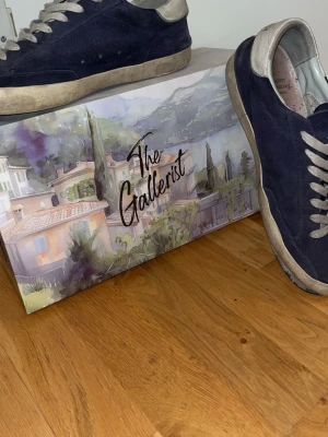 Mörkblå sneakers från The Gallerist - Snygga mörkblå sneakers från The Gallerist med vita skosnören och en unik vit klöverdetalj på sidan. Lådas får man om man köper och skorna har skador som är synliga på bilderna vilket gör att priset har sjunkit. Storlek 44