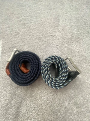 Två flätade bälten från Jack & Jones - Säljer två snygga flätade bälten från Jack & Jones. Ett är marinblått med bruna skinn-detaljer och det andra är randigt i blått, vitt och grått. Båda har silverfärgade metallspännen och är perfekta för att lyfta din outfit. Skickar i packet men funkar också att mötas upp. Saddler bälte ordinarie pris 600kr och Jack & Jones 250kr. Säljer båda för 175kr men packet pris på 300kr.