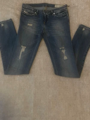 Diesel jeans 11-12år - Säljer ett par blå jeans från Diesel med slitningar på både fram- och baksida. Jeansen har klassisk femficksmodell, normal midja och smal passform. Materialet är denim med en snygg tvättad look och slitna detaljer för en trendig vibe.