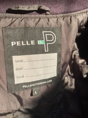 Svart bomberjacka från Pelle P - Snygg svart bomberjacka från Pelle P med guldfärgade dragkedjor och ribbade muddar vid ärmslut och krage. Jackan har tre fickor med dragkedja och en diskret logga på ärmen. Materialet är slitstarkt och har en lätt glansig finish.