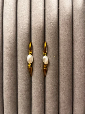 Guldörhängen med pärlor och konhänge - Snygga örhängen i guldfärgad metall med vita pärlor och ett hängande konformat smycke. Örhängena har en modern och trendig look med mix av klassisk pärla och edgy metallspets. Perfekta för dig som gillar att sticka ut med dina accessoarer.