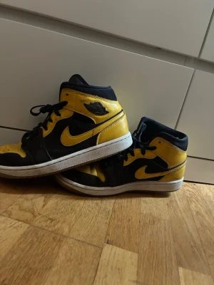Nike Air Jordan 1 Mid svart/gul - Säljer ett par Nike Air Jordan 1 Mid sneakers i svart och gul med vita sulor. Klassisk Jordan-logga på sidan och tungan. Skorna har en hög siluett och är tillverkade i läder med perforerade detaljer på tån för extra ventilation. Snygga och ikoniska sneakers för dig som gillar streetwear.
