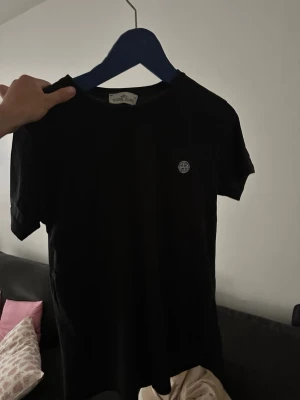 Svart t-shirt från Stone Island - Svart t-shirt från Stone Island med rund hals och liten logotyp på bröstet. Klassisk passform och korta ärmar, perfekt för en stilren och enkel look. Tillverkad i mjuk bomull som känns skön mot huden.