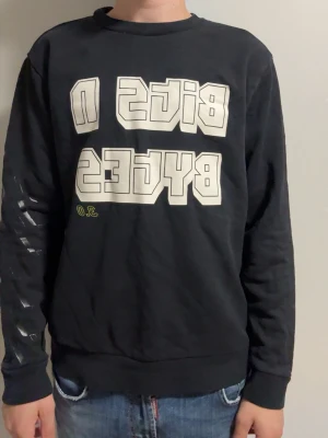 Svart sweatshirt med tryck från Hugo boss  - Cool svart sweatshirt med stort vitt tryck 'BIGS N BYCES' på bröstet och diskreta detaljer på ena ärmen. Tröjan har rund halsringning och ribbade muddar vid ärmslut och nederkant. Perfekt för en avslappnad streetwear-look.