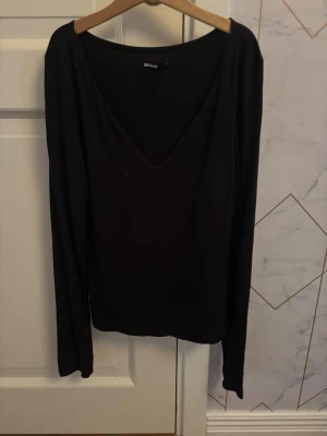 Svart långärmad topp Bik Bok - En svart långärmad topp från Bik Bok med djup v-ringning. Enkel och stilren design som passar till många olika outfits. Tillverkad i mjukt material för en bekväm känsla.