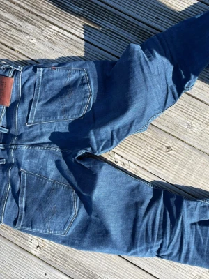 Replay ljusgrå slitna jeans - Säljer ett par ljusgrå jeans från Replay med slitningar och detaljerade sömmar. Jeansen har fem fickor, knappgylf och en klassisk passform. Perfekta för dig som gillar en avslappnad och trendig look.
