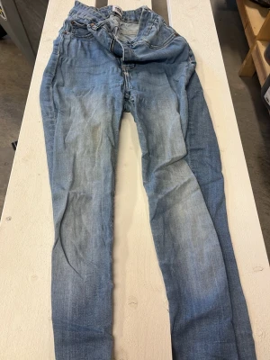 Ljusblå skinny jeans från 15% - Säljer ett par ljusblå skinny jeans från märket 15%. Jeansen har klassisk femficksdesign, normalhög midja och slitningar framtill för en avslappnad look. Tillverkade i mjukt denimtyg med gul kontrastsöm längs kanterna.