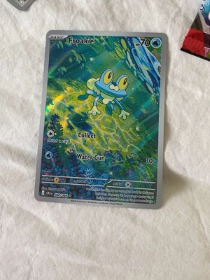 Pokémonkort Froakie holo#pokemon go #pokemon kort - Säljer ett holografiskt Pokémonkort med Froakie-motiv. Kortet har en färgglad design med blå, grön och gul bakgrund och Froakie i mitten. Kortet är gjort av laminerad kartong och har attackerna Collect och Water Gun. Perfekt för samlare eller Pokémonfans.