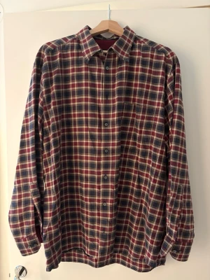 Rutig långärmad/oversized skjorta i bomull - Klassisk rutig skjorta i rött, blått och vitt. Skjortan har lång ärm, knappar framtill och en avslappnad passform. Perfekt för dig som gillar en tidlös och chill stil. Storlek: 43/44