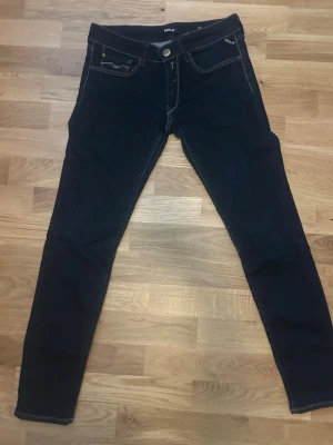 Mörkblåa skinny jeans från Replay - Snygga mörkblåa skinny jeans från Replay med klassiska fem fickor och kontrastsömmar. Jeansen har en smal passform och är tillverkade i stretchigt material för extra komfort. Perfekta för en trendig och avslappnad stil.