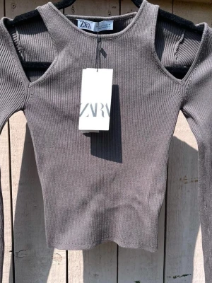Ribbad grå långärmad topp från Zara - Trendig ribbad topp från Zara i mörkgrå nyans. Långärmad modell med coola cut-out detaljer.  Materialet är mjukt och stretchigt, vilket gör den superbekväm. Den är S men sitter som en xs, snygg till fester