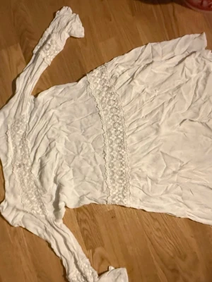 Vit långärmad klänning med spets - Romantisk vit klänning med långa ärmar och vackra spetsdetaljer vid midjan och ärmsluten. Klänningen har en feminin och mjuk siluett, perfekt för dig som gillar en bohemisk stil. Materialet känns lätt och luftigt.