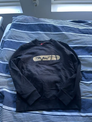 Svart sweatshirt från Hugo Boss - Snygg svart sweatshirt från Hugo Boss med tryckt beige logga på bröstet. Tröjan har rund halsringning, långa ärmar och ribbade muddar vid ärmslut och nederkant. Perfekt för en avslappnad och trendig stil.