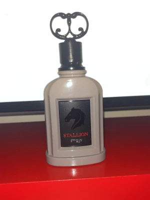 Stallion parfym 100ml från Zimaya - Snygg parfymflaska i grått med svart och röd etikett, dekorerad med en häst och texten Stallion. Flaskan har en unik, dekorativ svart kork och rymmer 100 ml Eau de Parfum. Tillverkad i Förenade Arabemiraten.