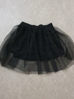 Kjol - En svart kjol i tyll med små glittriga guldprickar och bred resår i midjan. Kjolen har flera lager för extra volym och en festlig känsla. Perfekt för dig som vill sticka ut med en cool och trendig look.