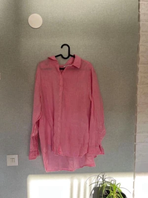 Rosa linneskjorta från Wera - Säljer en ljusrosa skjorta från Wera i 100% linne. Skjortan har klassisk krage, knappar framtill och långa ärmar. Perfekt oversized look och superfräsch färg som passar till många olika outfits.