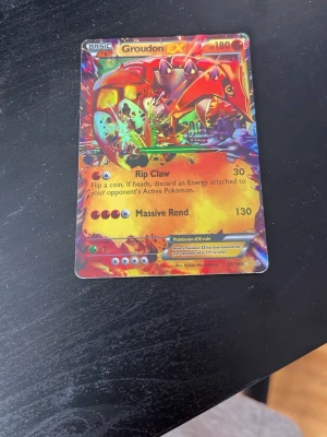 Pokémonkort Groudon EX holo - Säljer ett Pokémonkort Groudon EX med holografisk yta. Kortet har färgstark design med röd, gul och orange bakgrund och visar Groudon. Det är ett samlarkort från Pokémon-serien, nummer 85/160.