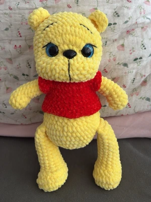 Gosedjur Nalle med röd tröja - Mjuk och gosig nallebjörn i gul plysch med stora blå ögon och svart nos. Nallen har en röd tröja och är handgjord med struktur i materialet. Perfekt som present eller dekoration i sovrummet. 30 cm hög