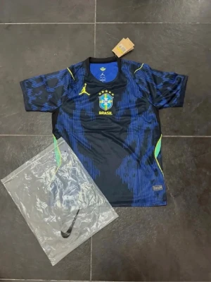 Blå Brasilien fotbollströja Nike Jordan - Snygg blå och svart Brasilien fotbollströja från Nike Jordan med officiellt klubbmärke och gula detaljer. Tillverkad i Dri-FIT material som andas, perfekt för träning eller match. Kortärmad modell med modern design och coola grafiska mönster.