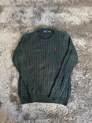 Mörkgrön kabelstickad tröja Polo Ralph Lauren (Medium) - 🟩 Ralph Lauren kabelstickad tröja Säljer denna superstirena, helt oanvänd kabelstickade tröja från Polo Ralph Lauren i en puderblå färg. Väldigt clean och enkel att styla till både jeans och cargos. Broderad logga på bröstet. ✨ Bra skick ✨ Mjuk och skön passform ✨ Perfekt för höst/vinter ✨ Storlek: Medium.