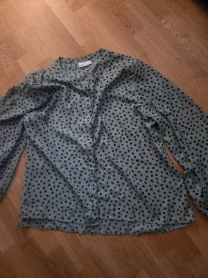 Grönprickig blus från isolde - Snygg grön blus med svarta prickar från isolde. Blusen har lång ärm, rund halsringning och knäppning framtill. Perfekt för dig som gillar mönstrat och vill ha en luftig och trendig look.