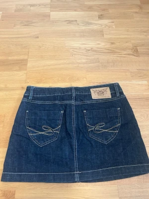 Mörkblå jeanskjol från edc by Esprit - Mörkblå jeanskjol från edc by Esprit med klassiska fickor fram och bak, kontrastsömmar och knappstängning. Snygg och enkel modell som passar till många olika stilar. Tydlig logga på baksidan i läderpatch.