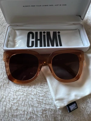 Bruna solglasögon från CHIMI - Snygga solglasögon från CHIMI med fyrkantig form och transparent brun båge. Glasen är mörka och ger en cool kontrast till den bruna ramen. Kommer med originalfodral och putsduk med CHIMI-logga. Perfekta för soliga dagar och trendiga outfits.