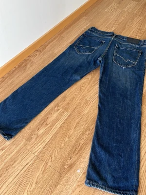 Blå raka jeans från Wrangler w32 L32 - Säljer ett par klassiska blå jeans med raka ben och tydliga kontrastsömmar. Jeansen har två bakfickor med den ikoniska Wrangler-sömmen och en svart patch i midjan. Tillverkade i slitstark denim, perfekta för en avslappnad stil. Jeansen är från crocker och är i väldigt bra skick säljer för dem var får små