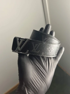 Svart bälte - Snyggt svart skärp med klassiskt -spänne i metall och diskret monogrammönster över hela bandet. Skärpet är gjort i skinn och har en stilren look som passar till många outfits.