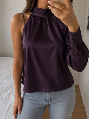 Mörklila oneshoulder topp med hög krage - Snygg mörklila oneshoulder topp med hög krage och ballongärm med knappar. Ena axeln har smalt axelband och den andra sidan har lång ärm. Tillverkad i ett glansigt, mjukt material som ger en lyxig känsla.