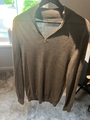 Grå halvzip-tröja från Studio Total - Snygg grå stickad tröja från Studio Total med halvzip och hög krage. Tröjan har långa ärmar och ribbade muddar vid ärmslut och nederkant. Perfekt för lager på lager och enkel att matcha med olika outfits.