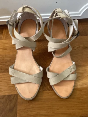 Beige pumps med remmar från Gant - Snygga pumps från Gant i ljust läder med korsade remmar och öppen tå. Smal klack i trälook och justerbart spänne vid ankeln. Trendiga och stilrena! Skorna är lite fläckiga längst bak (se sista bild) men det går säkert att få bort det mesta om man putsar de. 